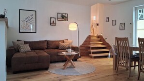 A living room with a brown sofa, a coffee table, a staircase, and a dining area with wooden chairs. - Ida vacation apartment - your temporary home in the Harz Mountains. (Quedlinburg)
