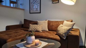 A cozy living room with a brown sofa, patterned cushions, a glass coffee table with a candle, and a framed artwork on the wall. - Ida vacation apartment - your temporary home in the Harz Mountains. (Quedlinburg)