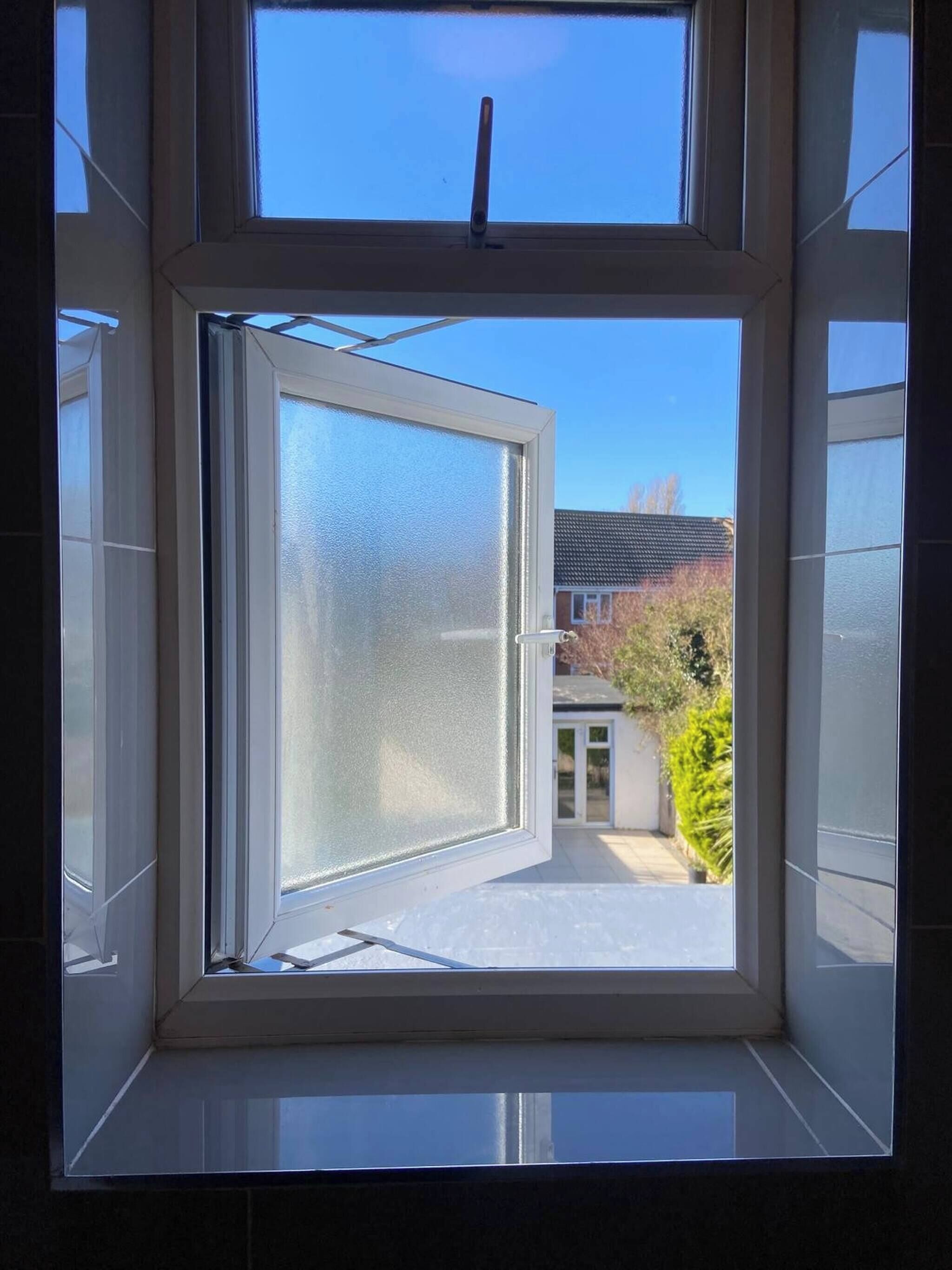A window with a view of a residential area, including a house and a pathway.