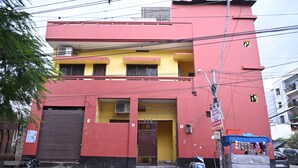 A two-story building with a red and yellow facade, a closed front door, and a small shop with a blue canopy. - The Ganga Guest House (Varanasi)