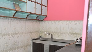 A kitchen with a pink wall, a sink, and cabinets. - The Ganga Guest House (Varanasi)