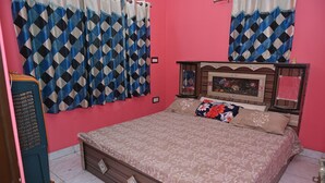 A bedroom with a bed, curtains, a dresser, and a small statue on the dresser. - The Ganga Guest House (Varanasi)