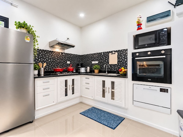 A modern kitchen with a stainless steel refrigerator, a microwave, an oven, and a black tiled backsplash.
