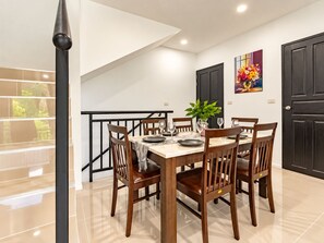 A dining area with a table set for four, surrounded by wooden chairs, a potted plant, and a painting on the wall. - Tropical Private pool villa Chalong Phuket (ตำบล ฉลอง)