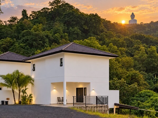 A modern two-story building with a flat roof, a balcony, and a view of a large Buddha statue in the background.