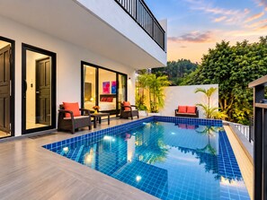 Ein moderner Poolbereich mit einem verglasten Schlafzimmer, Sitzgelegenheiten im Freien und üppigem Grün.