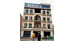 Un immeuble à plusieurs étages doté d’une entrée centrale, de balcons ornés de plantes et d’une enseigne au-dessus de l’entrée.