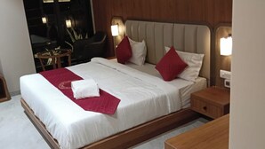 Un lit bien fait, avec du linge de lit blanc et des coussins rouges, une table de chevet et une petite table de nuit en bois.