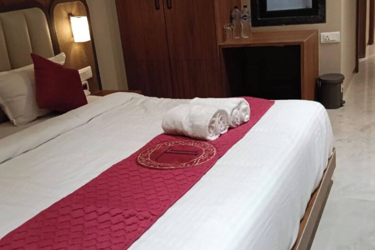 A neatly made bed with a red and white bedspread, a folded white towel, and a circular logo on the bedspread.