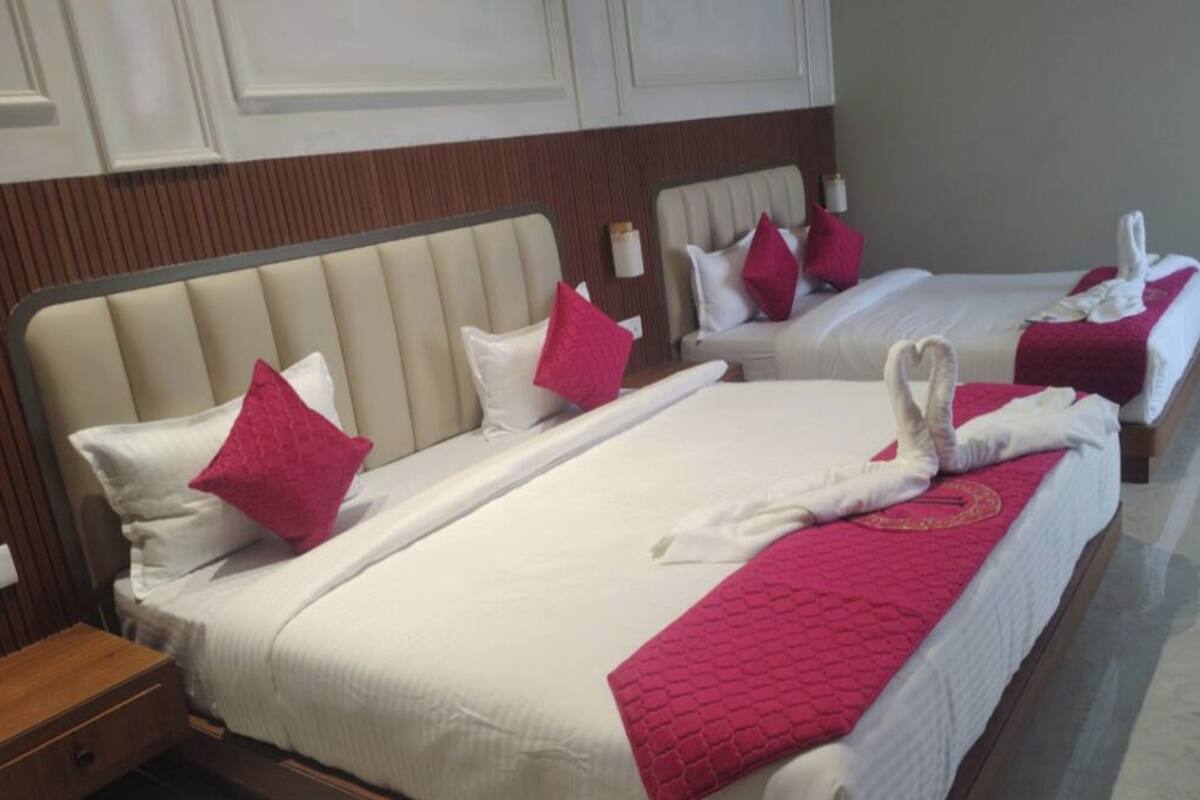 A hotel room with two beds, each with a white headboard, pink pillows, and towels.