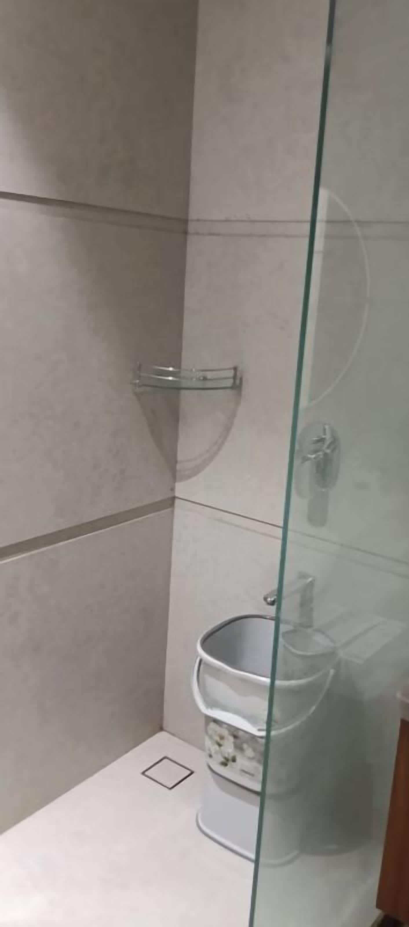 A glass-enclosed shower stall with a white bucket and a metal showerhead.