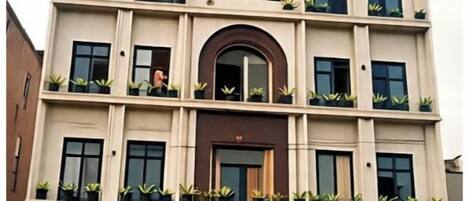 Un edificio a più piani con un ingresso centrale, balconi con piante e un cartello sopra l'ingresso.