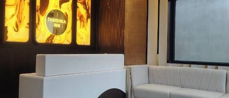 A modern interior with a white reception desk, a grey sofa, and a large screen wall.
