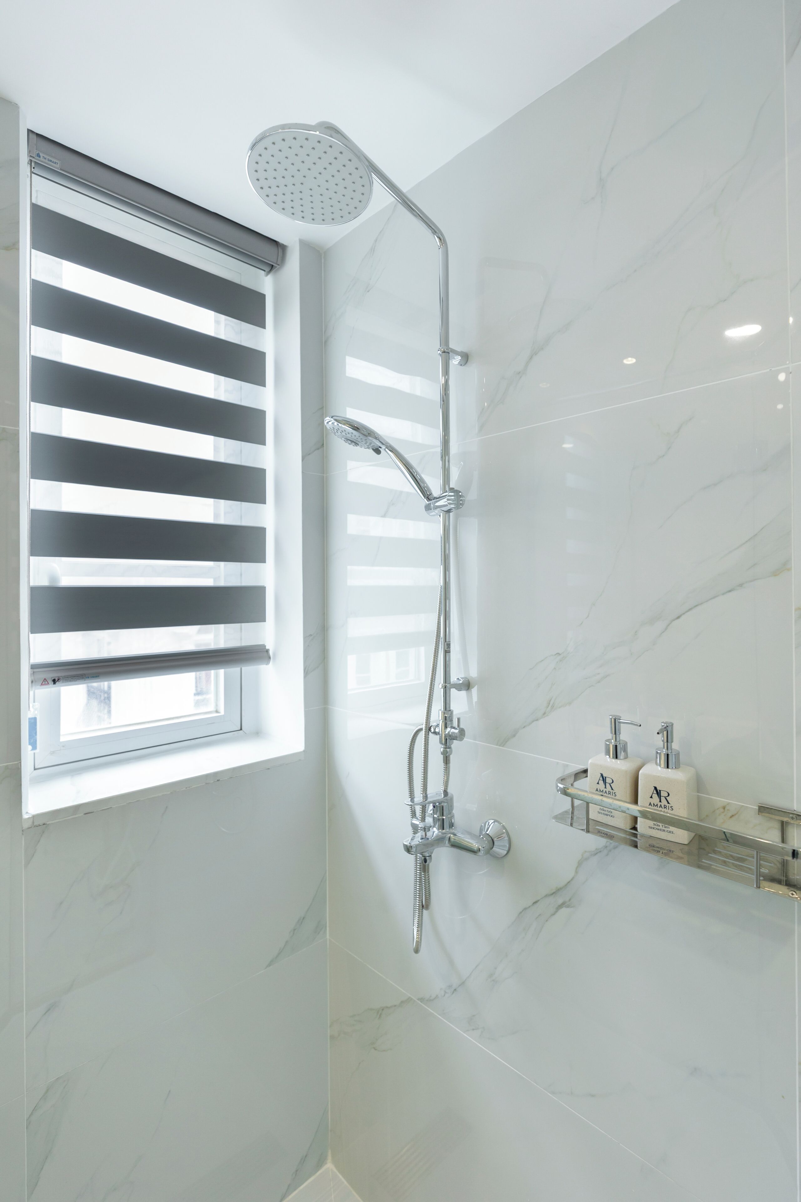 A modern bathroom with a shower, a window with blinds, and a marble wall.