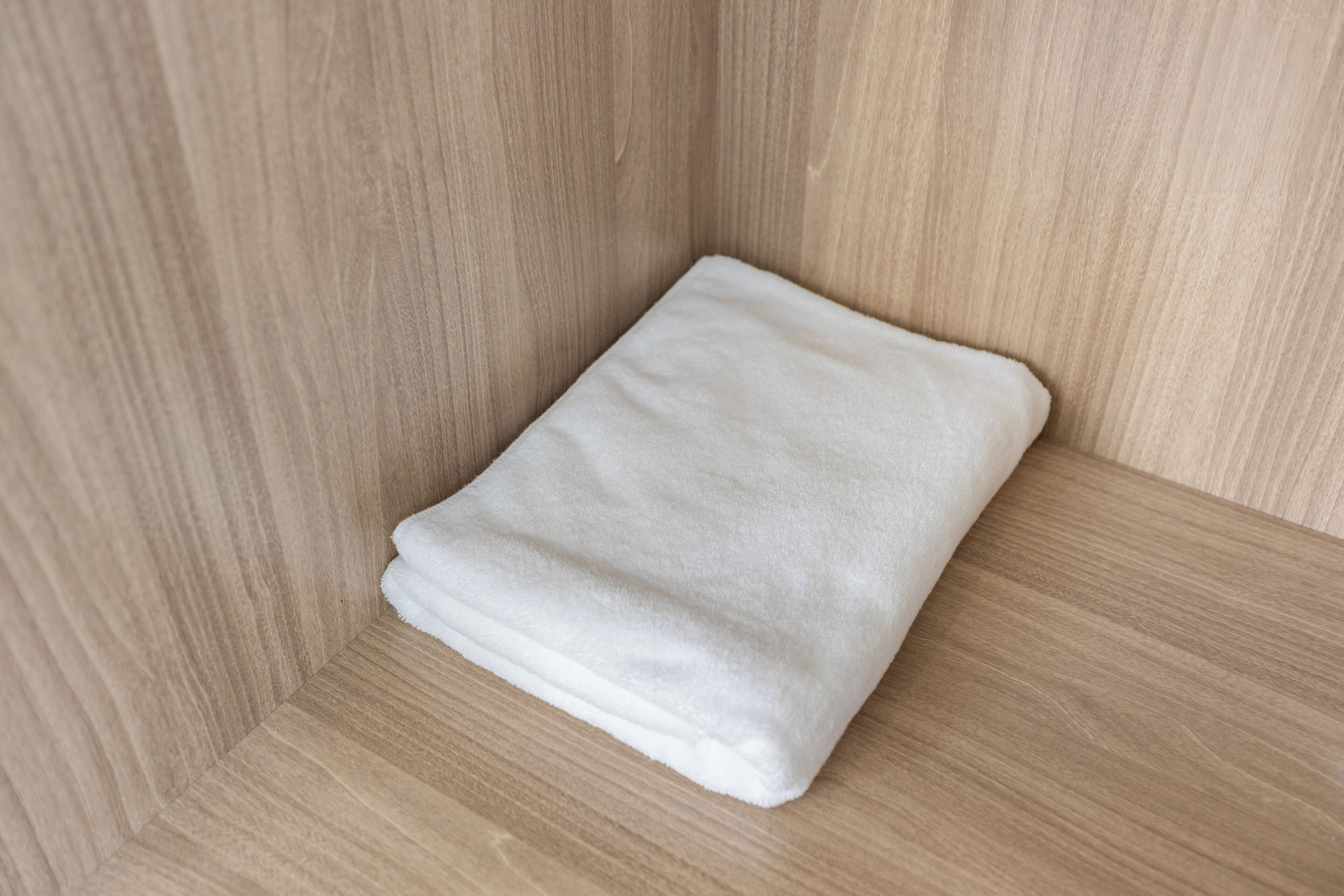 Una toalla blanca doblada con cuidado en un rincón de una habitación con paredes de madera clara.