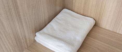 Una toalla blanca doblada con cuidado en un rincón de una habitación con paredes de madera clara.
