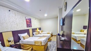 A hotel room with four beds, a large mirror, a flat-screen TV, and a wall-mounted clock.