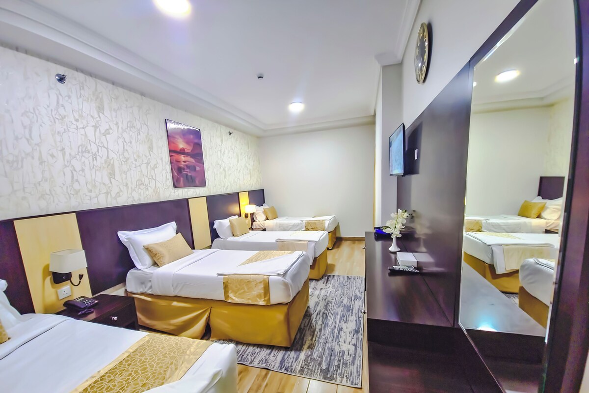 A hotel room with four beds, a large mirror, a flat-screen TV, and a wall-mounted clock.