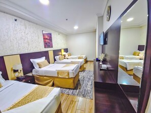 A hotel room with four beds, a large mirror, a flat-screen TV, and a wall-mounted clock. - Romance Elite Hotel (Makkah)