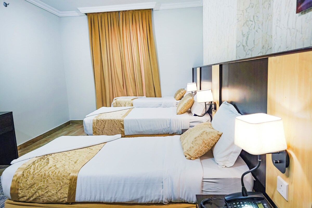 A hotel room with two beds, a bedside table with a lamp, a telephone, and a curtain.