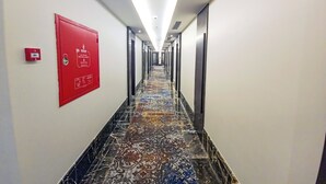 A hotel hallway with a patterned floor, a fire alarm on the left, and doors on both sides.