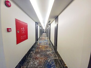 A hotel hallway with a patterned floor, a fire alarm on the left, and doors on both sides. - Romance Elite Hotel (Makkah)