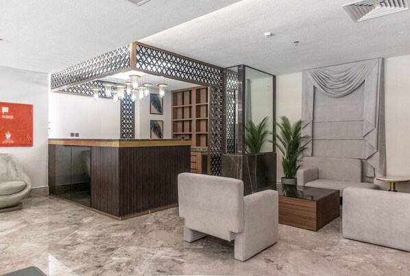 A modern lobby with a reception desk, seating area, and a decorative partition. - Romance Elite Hotel (Makkah)