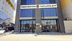 A hotel with a modern facade, large windows, and a sign indicating it is the Romanc Elite Hotel.