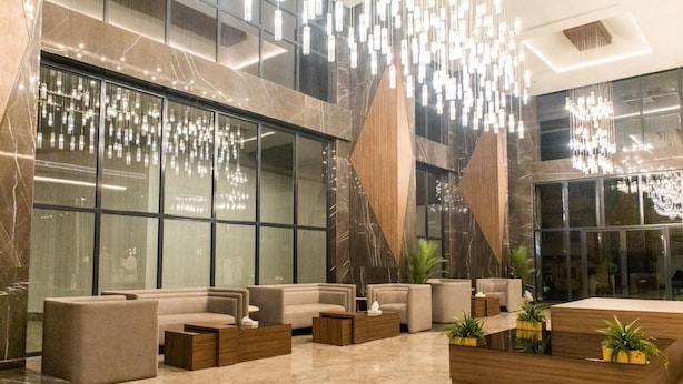 En rummelig lobby med et moderne design, der inkluderer et siddeområde med sofaer og et sofabord, en stor trævæg og hængende lamper.