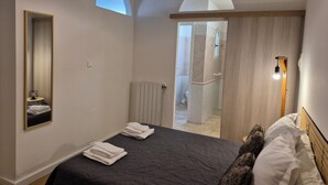 A modern bedroom with a large bed, a mirror, and a door leading to a bathroom. - LES AGRUMES (Lucciana)