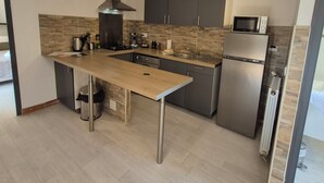 A modern kitchen with a central island, dark cabinets, and stainless steel appliances. - LES AGRUMES (Lucciana)