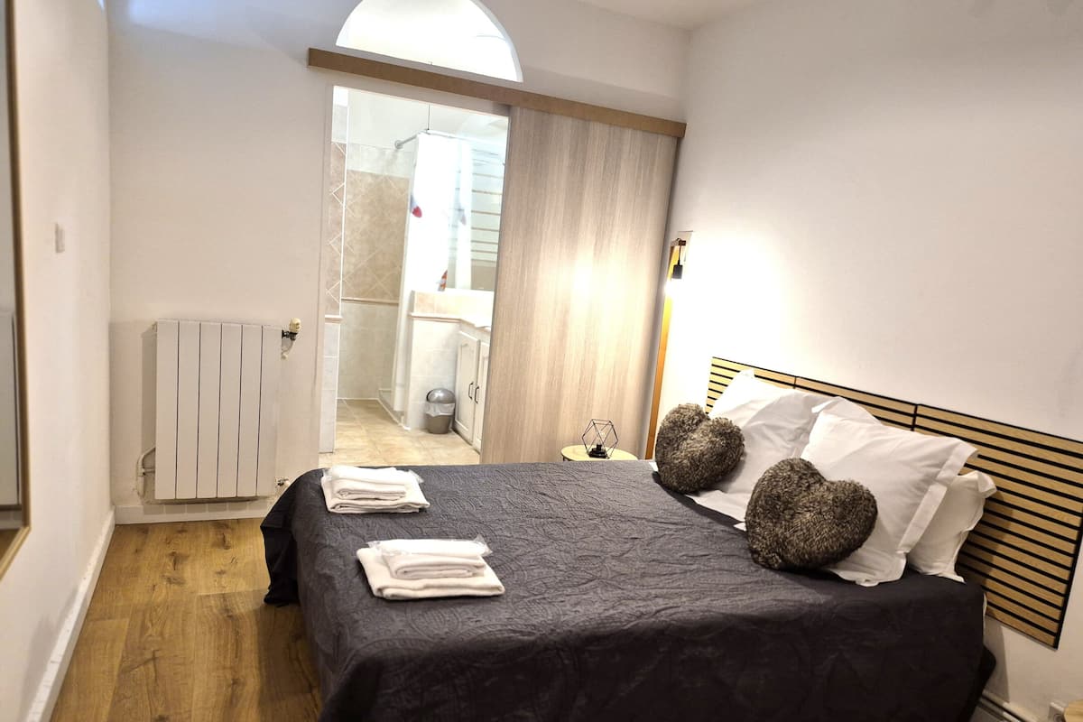 Ein ordentlich gemachtes Bett mit dunkler Bettdecke und weißen Handtüchern, ein Holz-Kopfteil und ein Nachttisch mit einer Lampe.