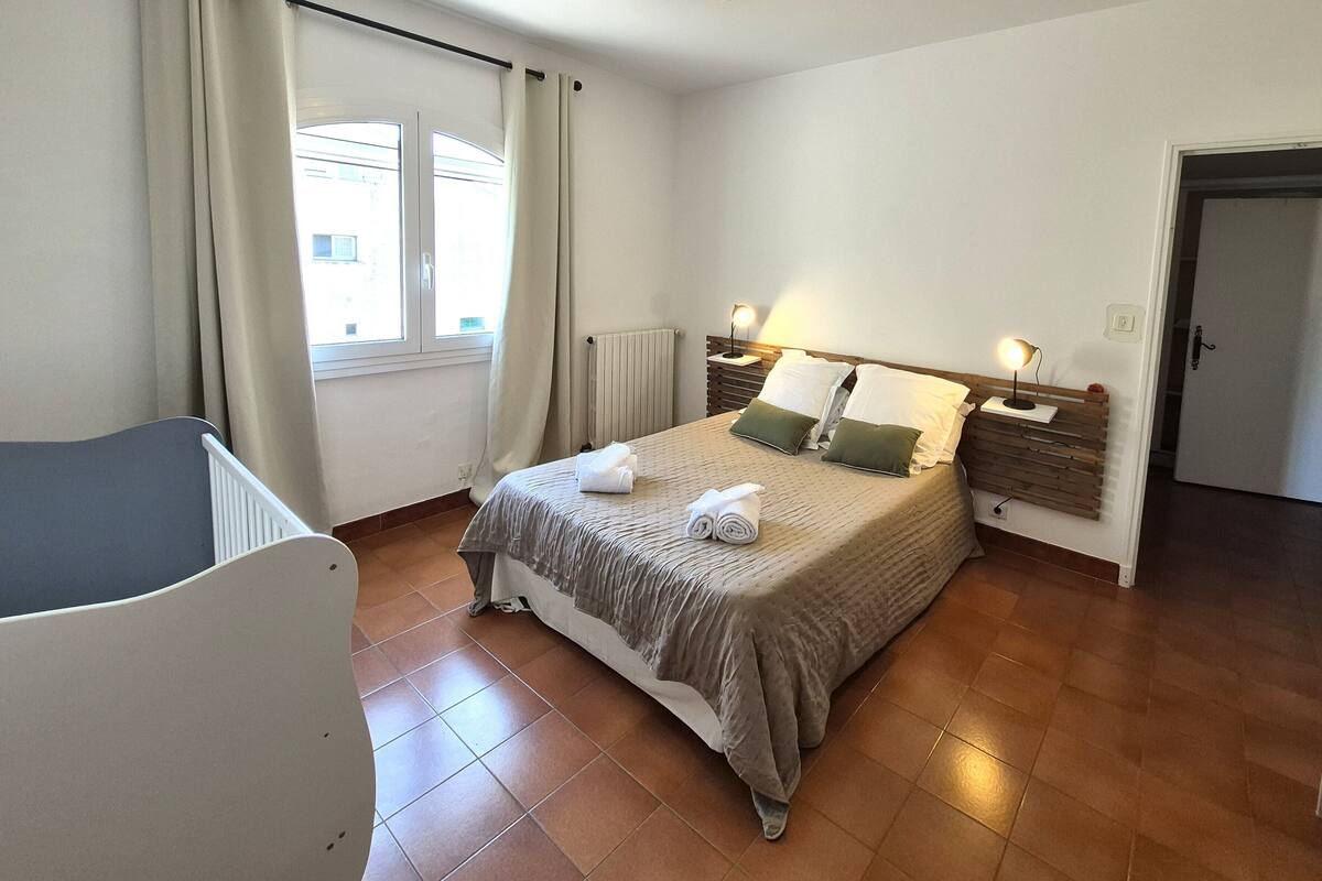 Ein ordentlich eingerichtetes Schlafzimmer mit Bett, Nachttischlampen, Heizkörper und einem Fenster mit Vorhängen.