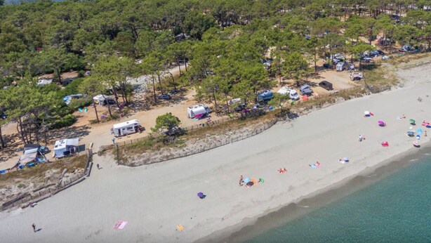 An aerial view of a beach with multiple RVs and tents, a sandy shoreline, and a clear view of the ocean. - LES AGRUMES (Lucciana)