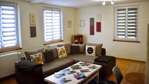 A living room with a sofa set, a coffee table with magazines, and a bookshelf. - Cosy gîte in renovated farmhouse. Spacious bedroom + living room. Pets allowed (Weitbruch)