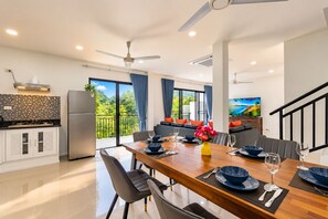 A modern kitchen with a refrigerator, dining table set for four, and a balcony with a view. - Tropical Private Pool Villa Phuket (ตำบล ฉลอง)