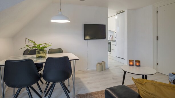 A modern living room with a dining area, a TV mounted on the wall, and a small table with candles. - Scandinavian Charm in Aalborg (Aalborg)