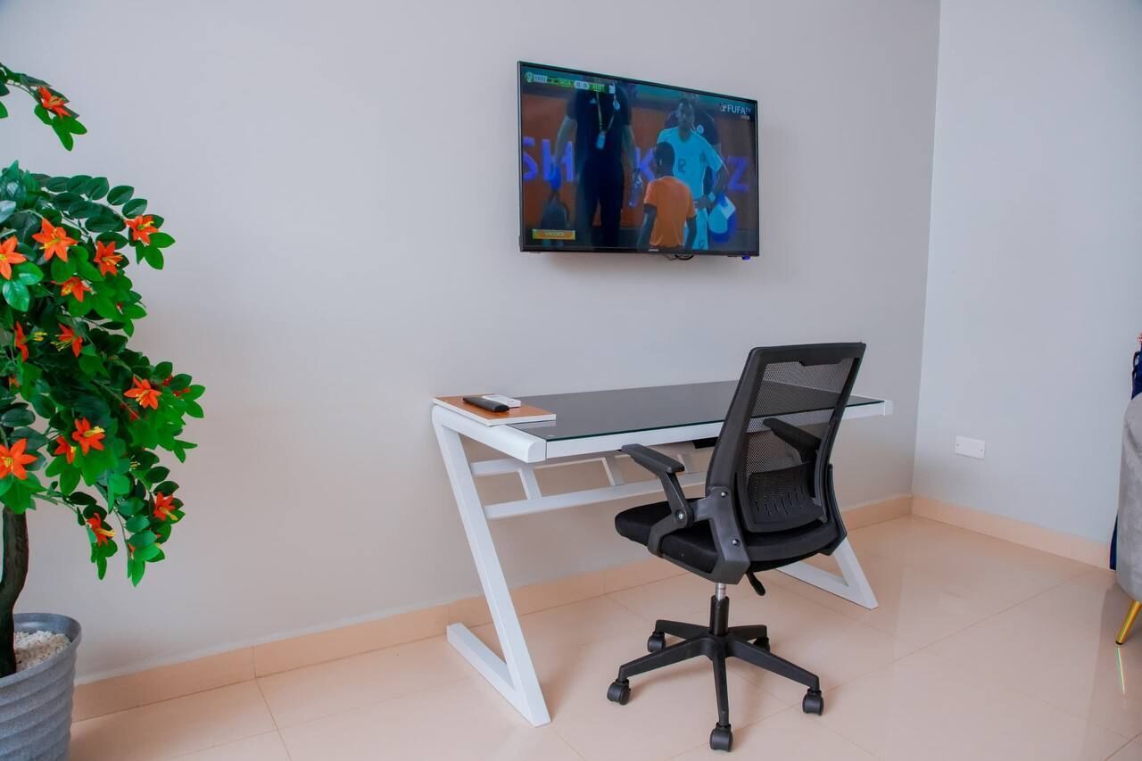 A modern office space with a white desk, black office chair, and a television mounted on the wall displaying a sports event.