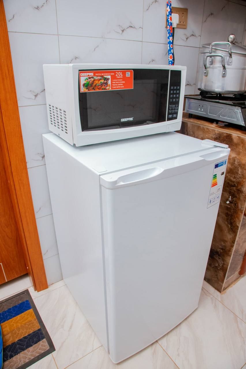 Una cocina compacta con un microondas blanco sobre un refrigerador blanco, estufa y un salpicadero de azulejos.