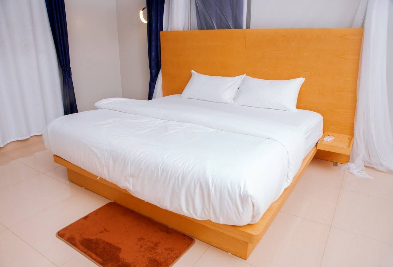 Un dormitorio moderno con estructura de cama de madera, ropa de cama blanca y una alfombra marrón.