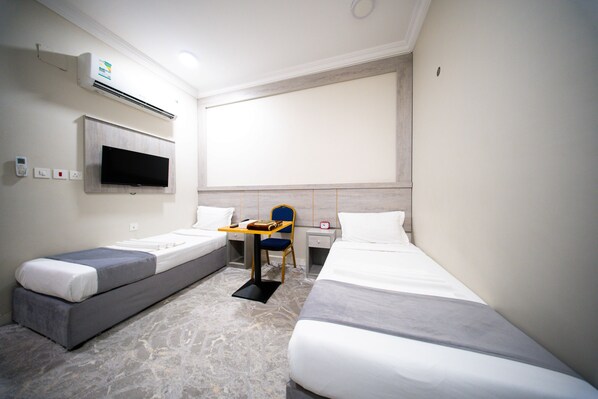 A hotel room with two single beds, a TV mounted on the wall, a desk with a chair, and a small table. - Rayhanat Almakan Hotel (Makkah)