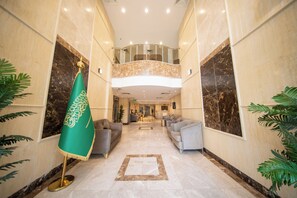 A spacious lobby with a high ceiling, marble flooring, and a seating area with sofas. A green flag with gold trim is visible on the left. - Rayhanat Almakan Hotel (Makkah)