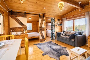 A cozy cabin interior with a wooden floor, a bed, a sofa, and a dining area.