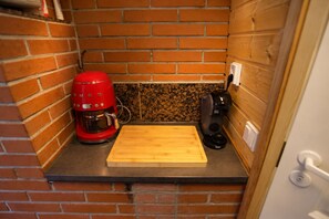 Eine kleine Küche mit einer Ziegelwand, einer roten Kaffeemaschine, einer schwarzen Kaffeemaschine und einem Holztisch.