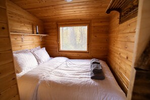 A wooden cabin room with a bed, a window, and a shelf. - Aurora River Cabin Ivalo – Hot Tub, Sauna & Cold Plunge (Inari)