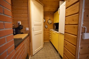 A compact kitchen with wooden walls, a white door, and yellow cabinets. - Aurora River Cabin Ivalo – Hot Tub, Sauna & Cold Plunge (Inari)