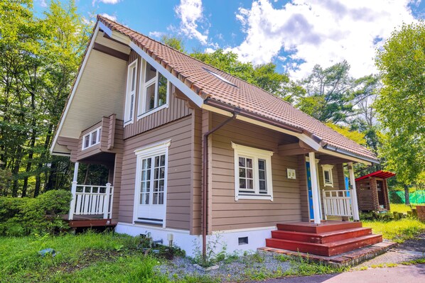 Une maison à deux étages avec un porche, une petite terrasse et un escalier rouge menant à la porte d’entrée.