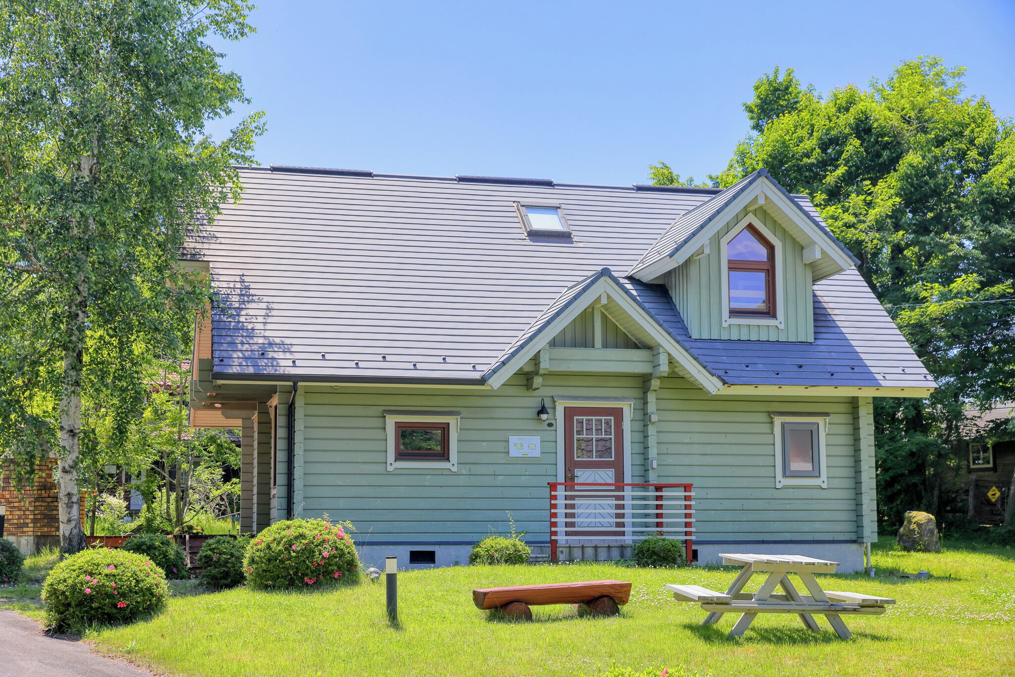 A small, single-story house with a gabled roof, a front porch, and a picnic table in the yard.
