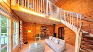 A wooden cabin interior with a sofa, ottoman, and a staircase leading to an upper level.