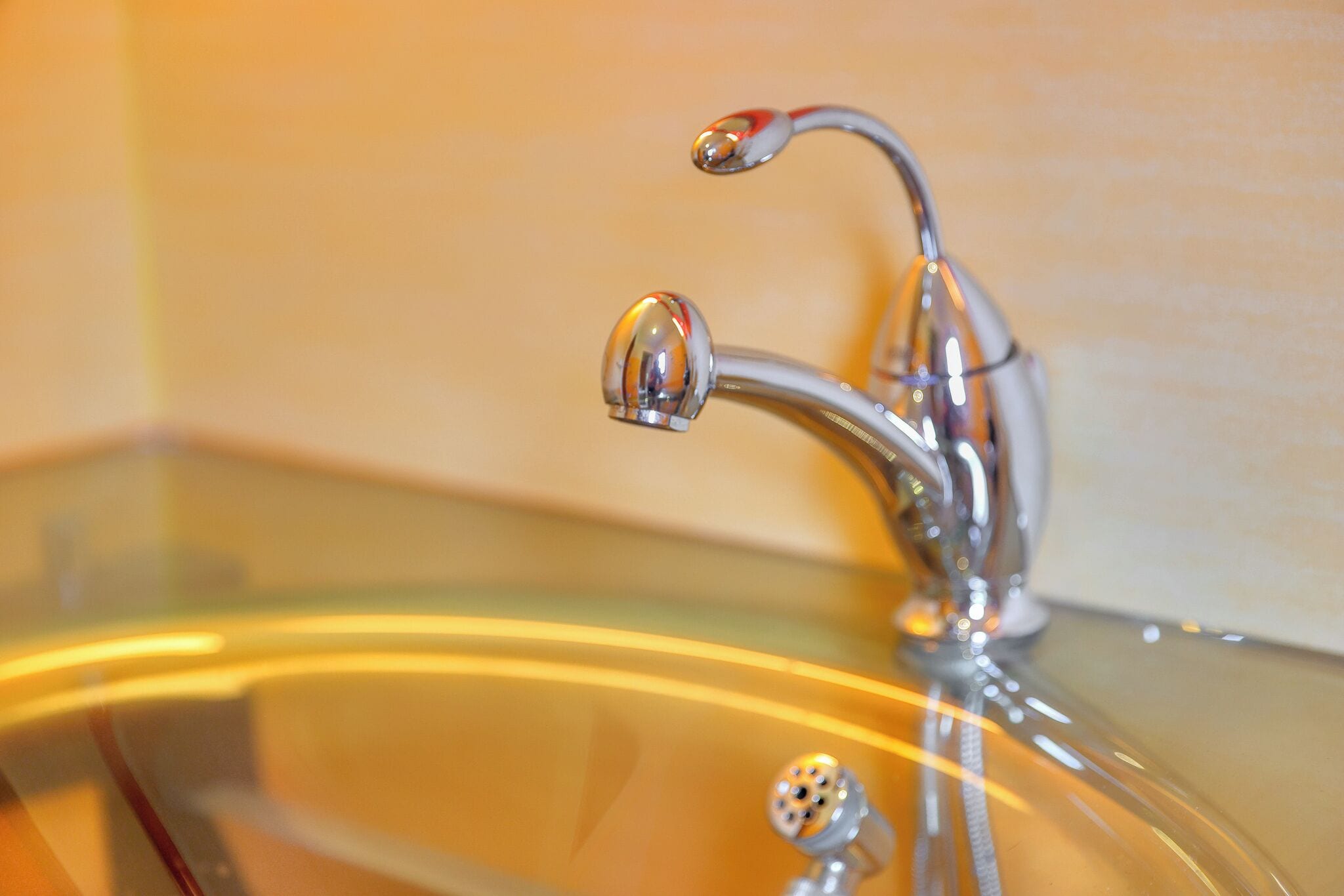 Un lavabo de salle de bain avec un robinet chromé et un bac en verre.